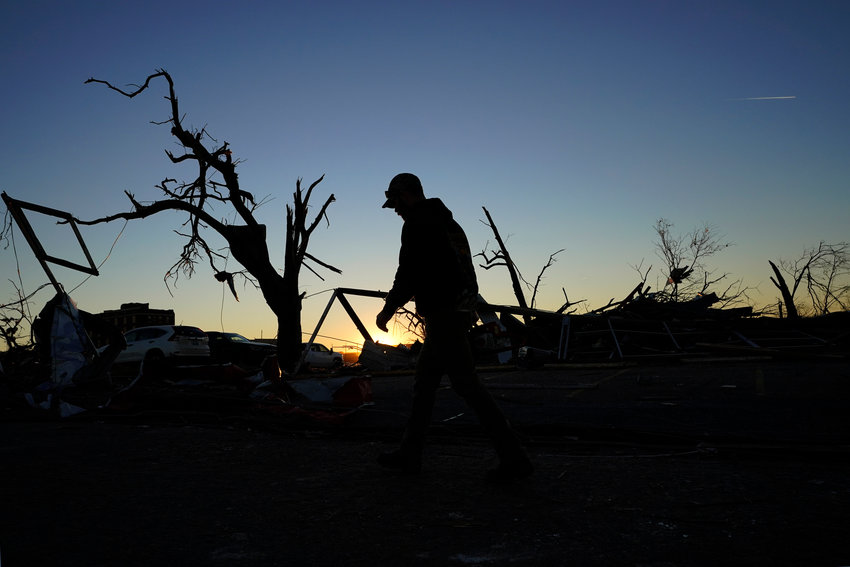 A cleanup worker walks past damaged trees and debris at the end of the day Sunday, Dec. 12, 2021, in Mayfield, Ky. Tornadoes and severe weather caused catastrophic damage across several states Friday, killing multiple people. (AP Photo/Mark Humphrey)