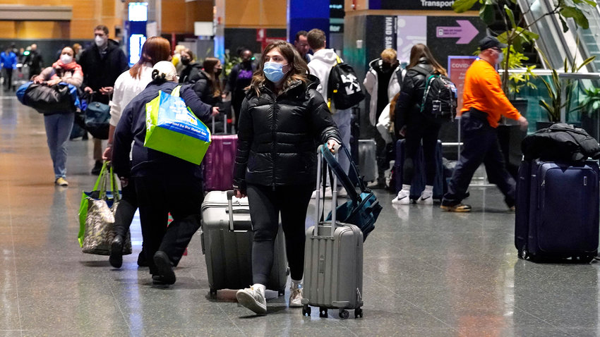 Travelers trek through Terminal E at Logan Airport, Tuesday, Dec. 21, 2021, in Boston. Public health officials are urging caution as the new omicron variant might become the dominant strain in the U.S. during the holiday break. (AP Photo/Charles Krupa)