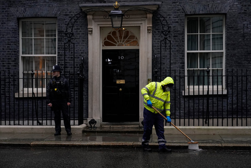 A worker sweeps in the rain and a police officer stands guard outside the door of 10 Downing Street, in London, Friday, Feb. 4, 2022. Four of Boris Johnson's most senior staff quit on Thursday, with a fifth staff member resigning on Friday morning, triggering new turmoil for the embattled British prime minister. Johnson's grip on power has been shaken by revelations that his staff held &quot;bring your own booze&quot; office parties, birthday celebrations and &quot;wine time Fridays&quot; in 2020 and 2021 while millions in Britain were barred from meeting with friends and family during coronavirus lockdowns. (AP Photo/Alberto Pezzali)
