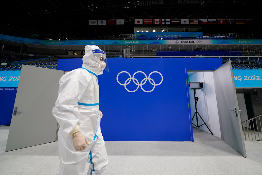 FILE - A worker in protective gear walks past the Olympic rings at the National Indoor Stadium at the 2022 Winter Olympics, Feb. 1, 2022, in Beijing. (AP Photo/Matt Slocum, File)