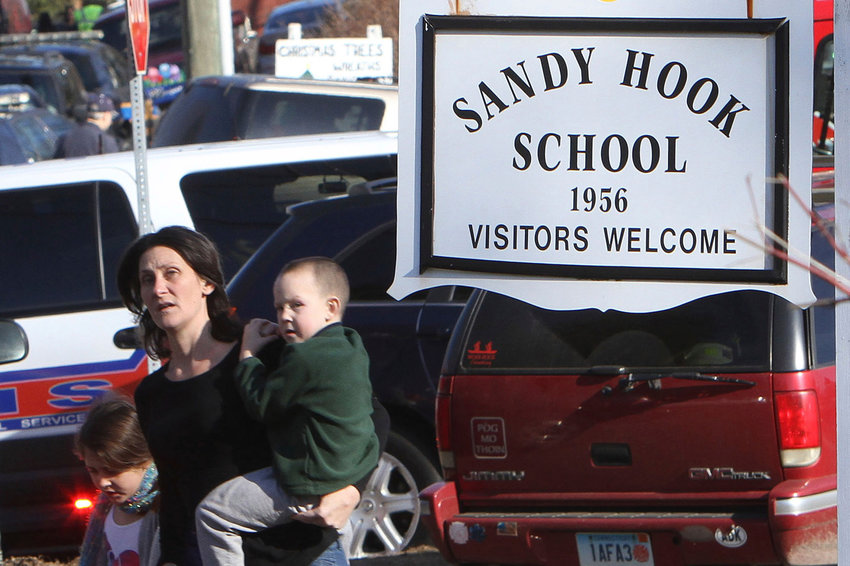 FILE &mdash; A parent walks away from the Sandy Hook Elementary School with her children following a shooting at the school in Newtown, Conn., Dec. 14, 2012. The families of nine victims of the Sandy Hook Elementary School shooting have agreed to a settlement of a lawsuit against the maker of the rifle used to kill 20 first graders and six educators in 2012, according to a court filing, Tuesday, Feb. 15, 2022. (Frank Becerra Jr./The Journal News via AP)