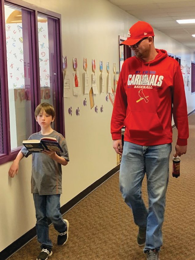 Third grader Remington Rains enjoys a book while walking with para Cody Freland.