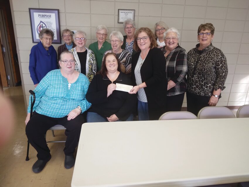 Pictured in the back row: Darlene Lamberson, Harriett Brust, Marjorie Sass, Sharolyn Moss and Pastor Nikena Ahart. Middle row: Vicki Maguire, Myrna Collins, Charlotte Burbridge and Renee Hack. Seated: Kris Gash and Director Christine Mether, with Lori Cohrs presenting the check. Not pictured: Norma Archer, Eleanor Gambs, Sharon Greenwood, Connie Leighton, Vicki Placek, Joyce Rosengren and Barbara Walters.