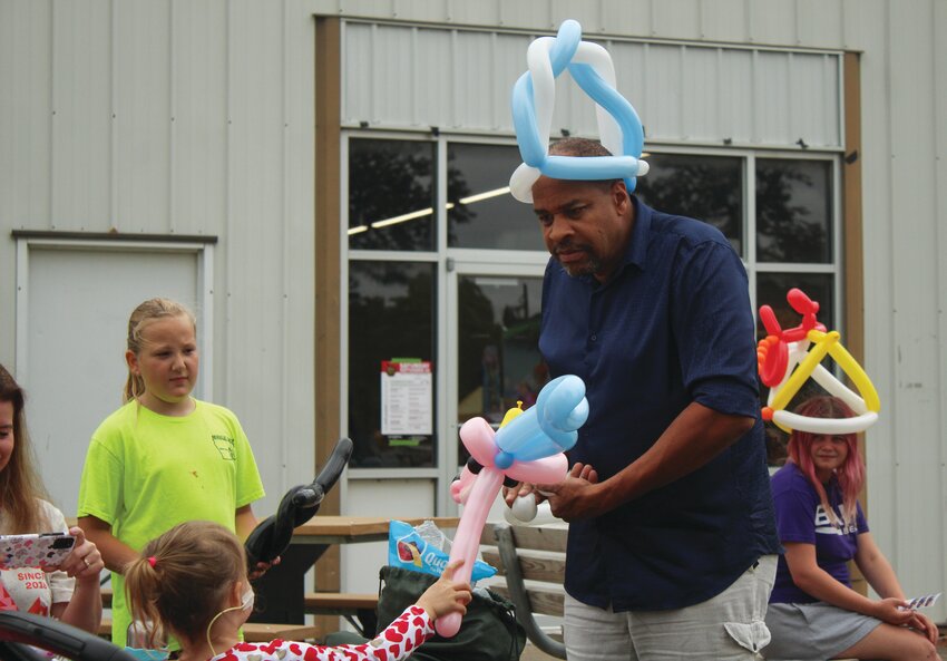 Anthony the Balloon Man makes a balloon sword while talking with kids and wearing one of his own balloon hats.