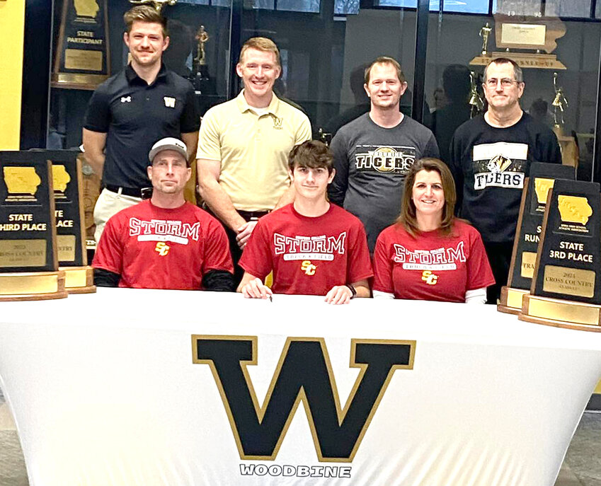 Woodbine's Owen Wingert (front, center) signed his letter of intent to continue his track career at Simpson College (Indianola), where he plans to pursue a degree in graphic design.  Wingert wrapped up his best cross country season, culminating in a Class 1A, 103rd place finish.  The Tigers have won three consecutive Class 1A third place finishes at the cross country meets (Fort Dodge), and were the Class 1A State Runner Up at State Track (2024) last spring. Shown in the front row (from left), Jake, Owen, and Trina Wingert.  Standing in the back row, Coach Ethan Hammerand, Coach Ryan Coenen, Coach James Smith, Coach Rod Smith.