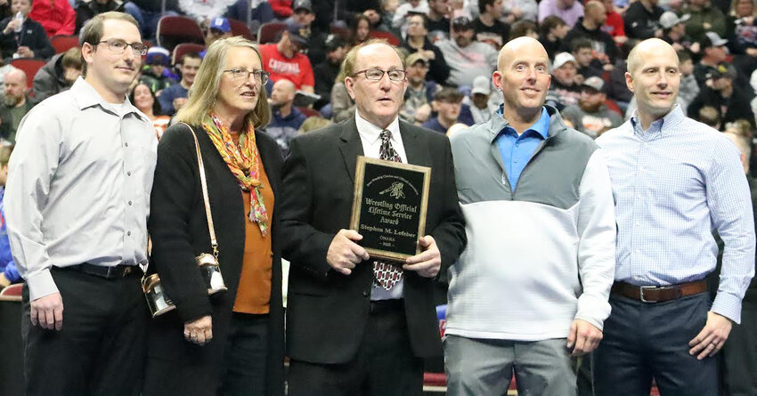 LIFETIME ACHIEVEMENT AWARD:  Tri-Center graduate Steve Lefeber received the 2025 Lifetime Achievement Award from the Iowa Wrestling Coaches and Officials Association on Feb. 22 at Wells Fargo Arena in Des Moines.  To receive this honor, he has dedicated over 40 plus years to the sport of wrestling, recruiting and mentoring new officials while promoting the sport, but since he lives in Omaha, Neb, he has never been selected as State Tournament Official at the Iowa High School Wrestling State Championships.  He is shown with his wife and family before the start of the Saturday Night State Finals.