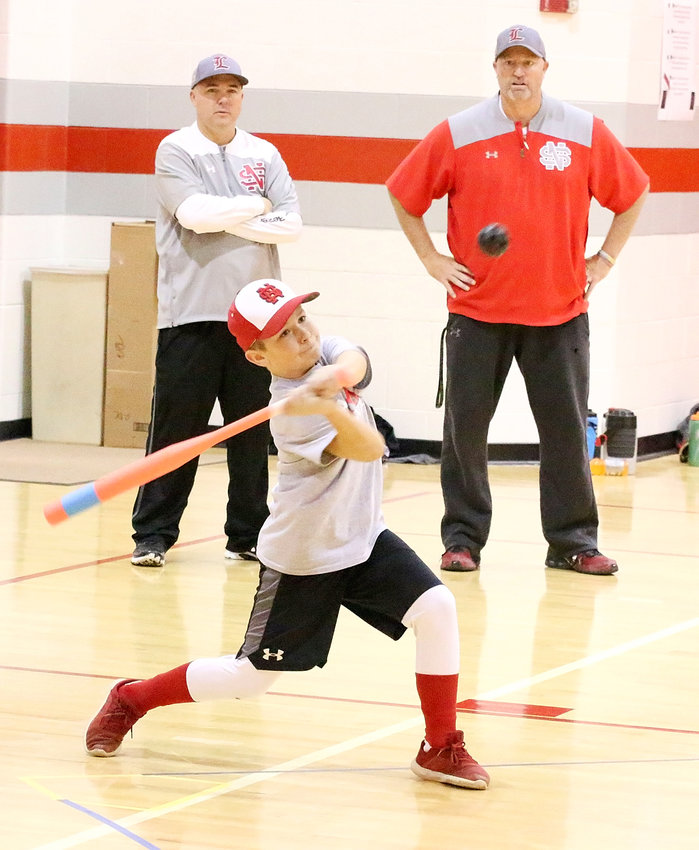 With North Scott baseball coaches Brad Ward and Travis Ralfs looking on, Kolton Engler shows off his power stroke during the 9th annual North Scott Wiffleball Tournament last month.