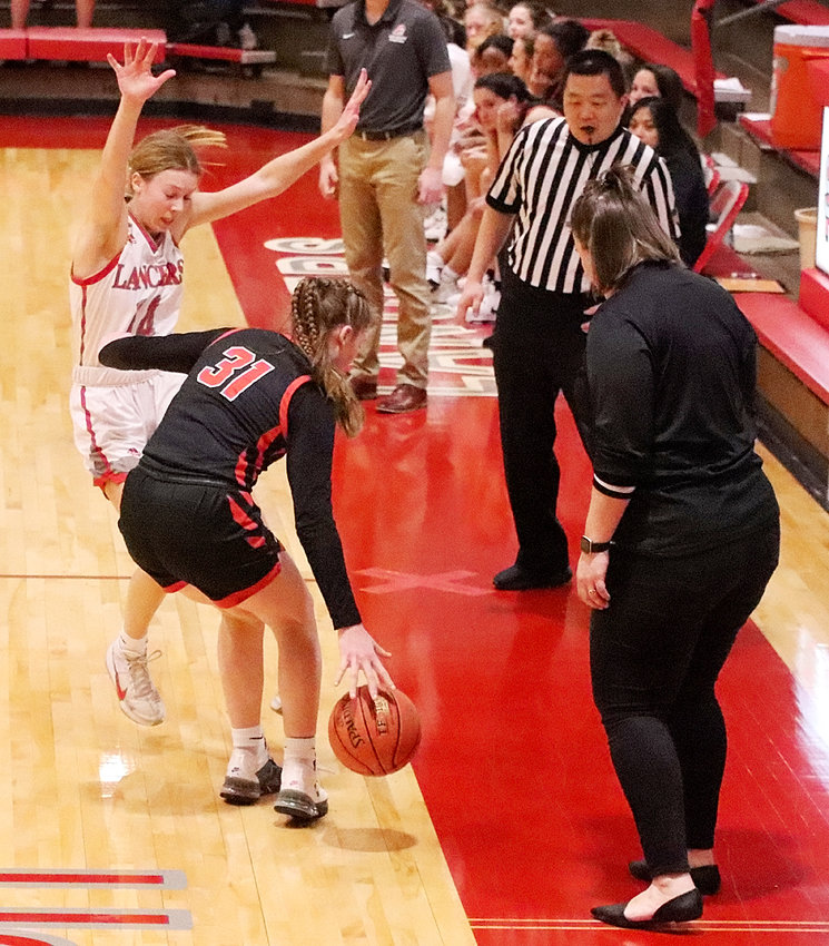 With Lancer coach Devvin Davis and the official keeping a watchful eye, junior Cora O'Neill displays tenacious defense and draws a charge during second-half action in the loss to Davenport Assumption.