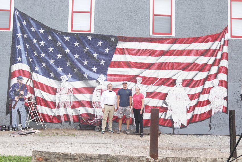 Candy Kitchen co-owner Lynn Ochiltree, Freedom Rock Artist Ray &quot;Bubba&quot; Sorensen, and Candy Kitchen co-owner Brenda Ochiltree stand in front of &quot;The Candy Kitchen Salutes... Duty, Honor, and Sacrifice&quot; while it is in the process of completion, July 26.