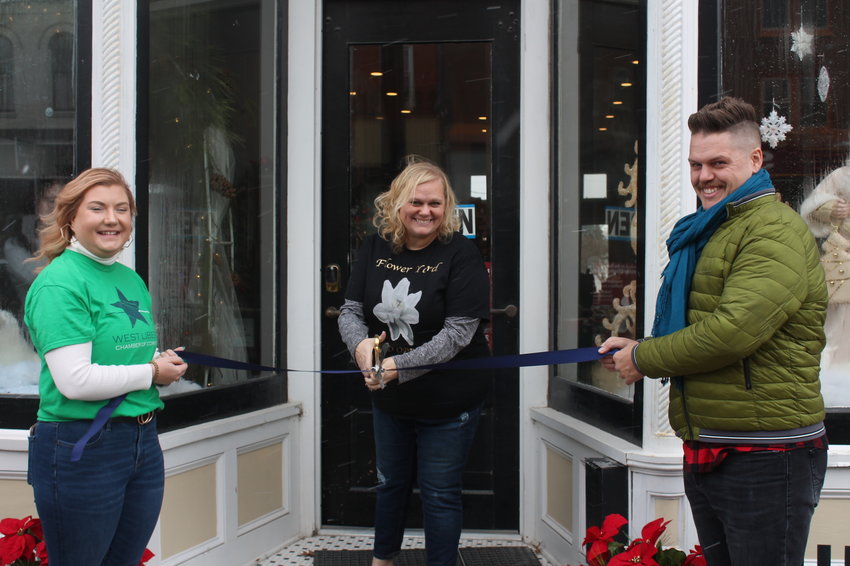 During the Holiday Open House, Flower Yard located at 116 East Third Street in West Liberty had its ribbon cutting. Pictured from left are West Liberty Chamber of Commerce boardmember Kayla Stumpf, Flower Yard business owner Destiny Brumbaugh and West Liberty Chamber of Commerce Director Charles Brooke holding the ribbon for Brumbaugh before the ribbon was cut.