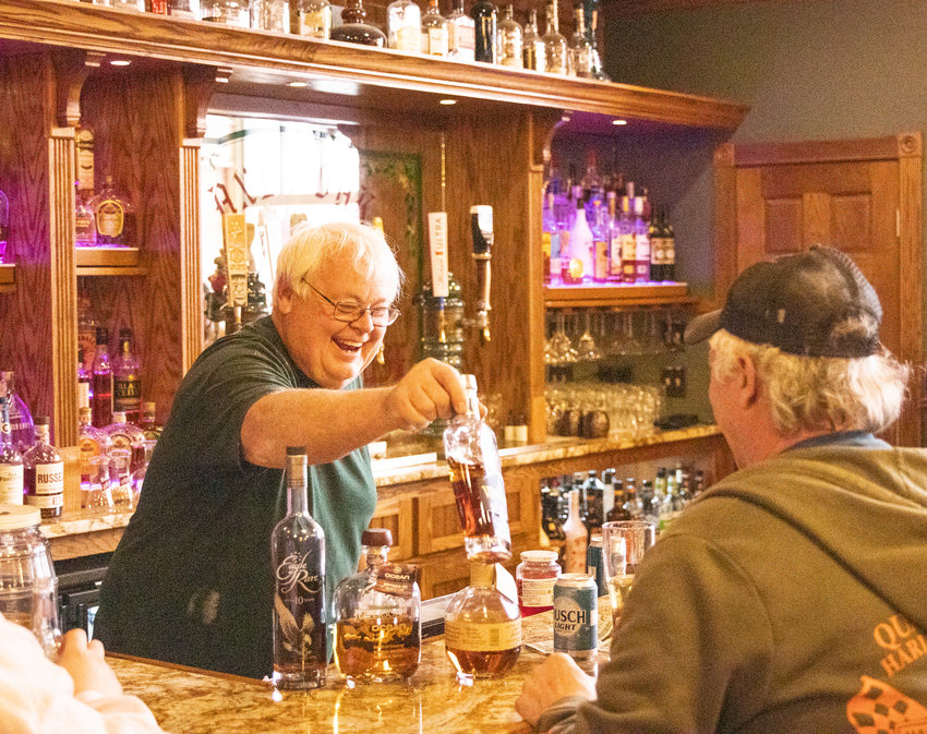 Axe &amp; Oak Whiskey House owner Fred Grunder laughs as he collects a bottle of whiskey from the bar.