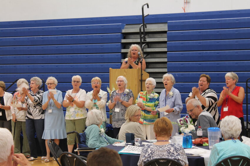 Pictured at the podium is Melody Henderson leading past cheerleaders in the West Liberty High School Comet Fight Song during the All School Reunion banquet Saturday, July 15, in the high school gymnasium.