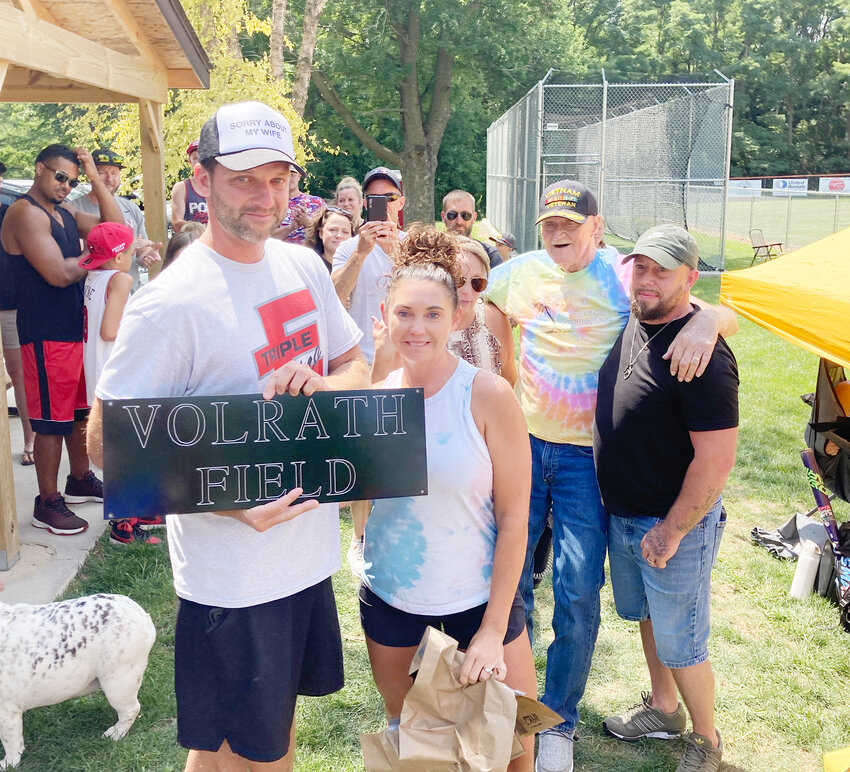 Travis and Casey Volrath pose with a new sign for the ball diamond at Woomert Park. That's former mayor and fire chief, Roger Woomert, in tie dye, who made the presentation, July 22.