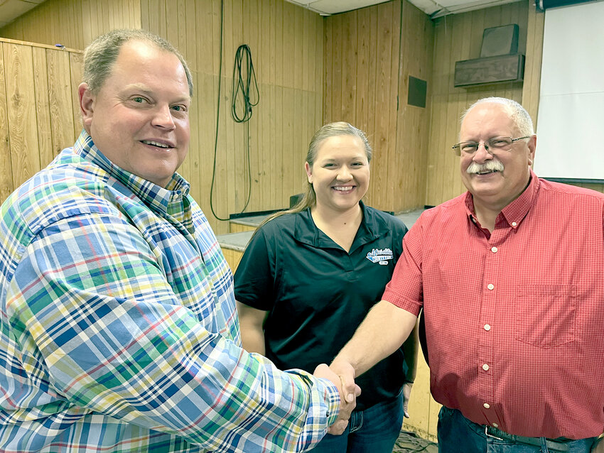 Former Muscatine County Fair Board President Troy Schlapkohl of Durant, on left, welcomes Steve Alt of West Liberty as the new president for the next two years, shadowed by Kelsey Meyers, fair manager.