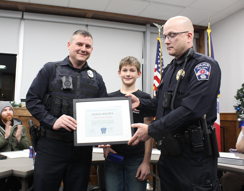 West Liberty Officer Derek Holmes, left, receives a life saving award from West Liberty Police Chief Don Strong, right.  Will Daufeldt the youth that Holmes saved, joins them for the Dec. 5 presentation at city hall. Photo by Jacob Lane