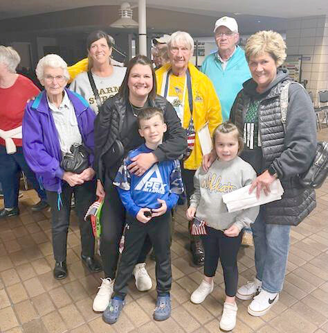 Bobby Bohnsack, center in yellow, is surrounded by family after returning from his Honor Flight. In front, granddaughter Erin DeLong with her kids, Grayson and Emma DeLong. In back, Jeanette Hoffmann, daughter Pam Hartwig, Bobby, son Rob Bohnsack, and sister-in-law Suzy Bohnsack.
