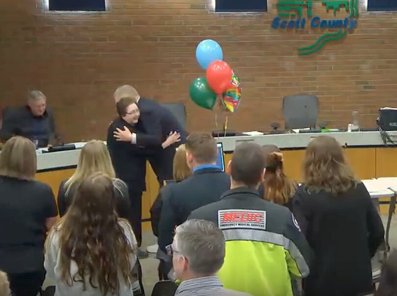 Sherry Burmeister gets a standing ovation from colleagues, and a hug March 11 from Scott County supervisor John Maxwell.
