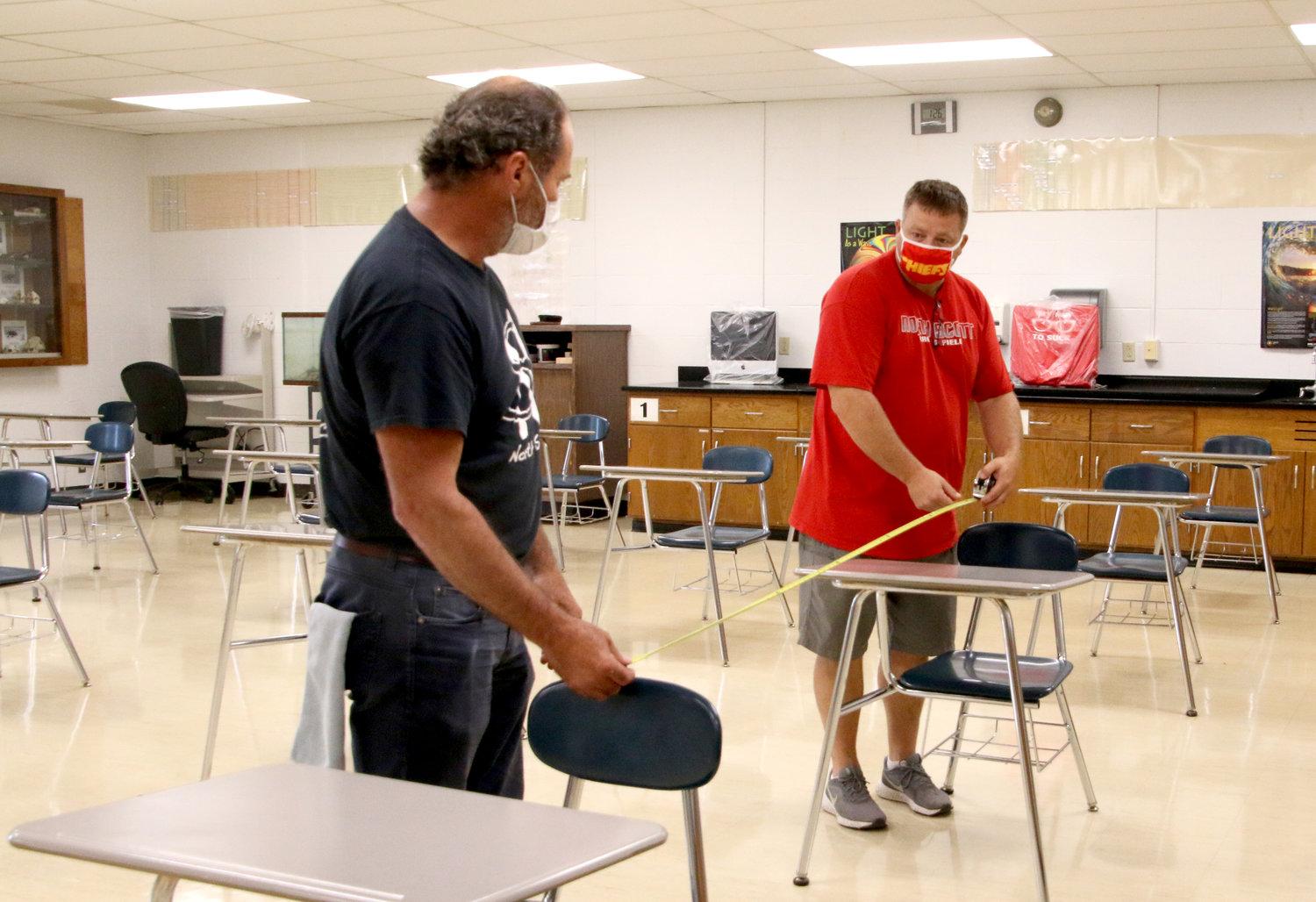 School district custodians Dan House, left, and Nate Noel, measure 6 feet between junior high classroom desks. The staff is removing non-essential tables, cabinets and other furniture to create enough room between desks.