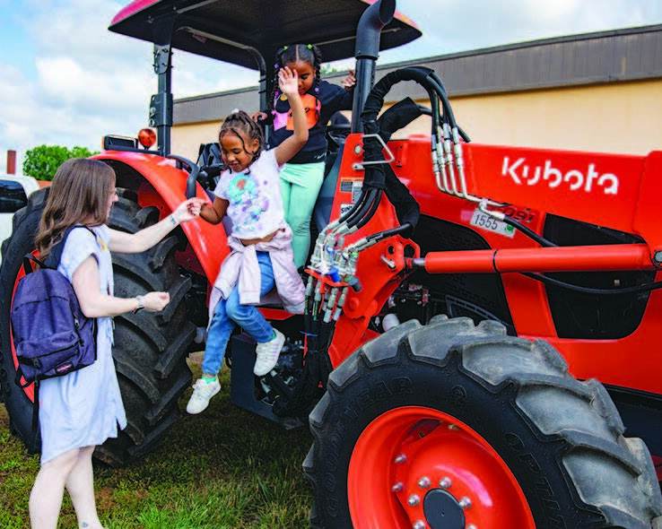 Rankin Elementary Kindergarten teacher Taylor Mirabella assists a student from a tractor at the school’s Careers on Wheels presentation. Photo by Ivan Saul Cutler/Carolina Peacemaker.