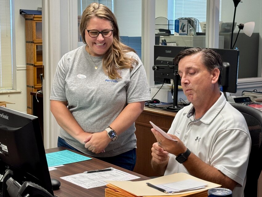 Perry County Clerk Jared Kutz opens an envelope containing an absentee ballot his office received through the mail while Perry County Treasurer Katie Schemel looks on.