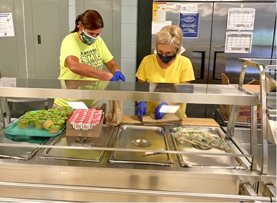 District 32 food service workers Kimberly Seabaugh and Charlotte Colin pack bagged meals for children, who eat free on any school day, either in school or by picking up Grab & Go Meals through the drive-thru line.