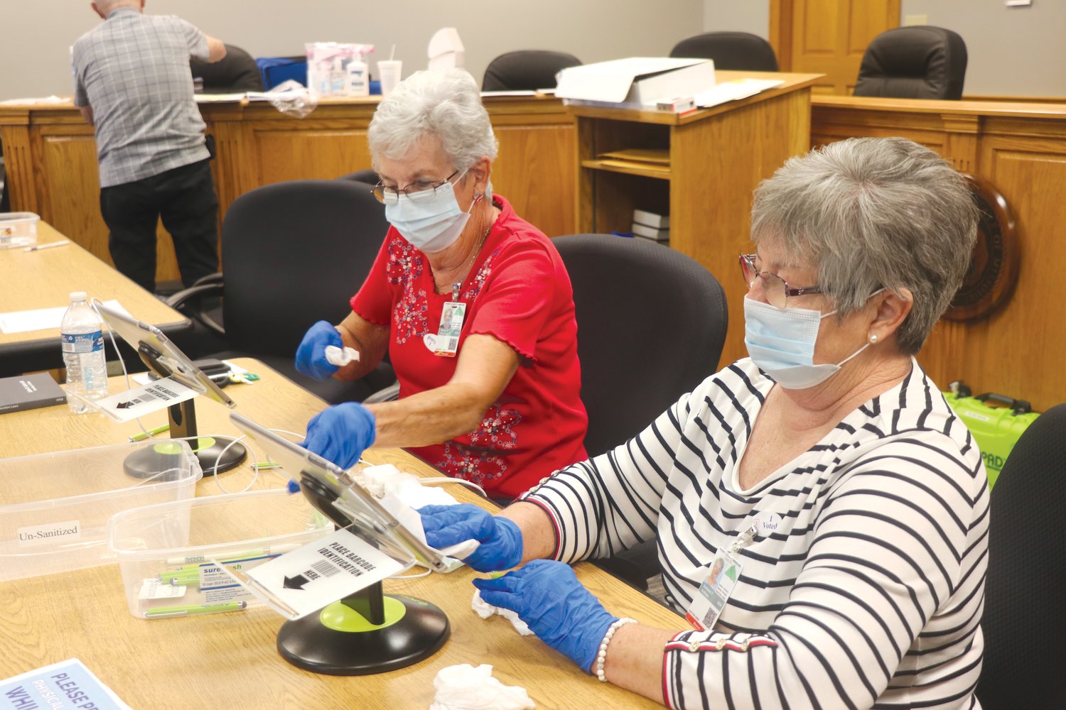 Perry County election workers Margie Winschel (left) and Kathy Hoffman disinfect and sanitize the pens and the sign-in screen as they wait between voters at City Hall during the August primary election on Aug. 4, 2020.  Voters at the polls for Tuesday's general election can expect to see the same public health protocols in place.