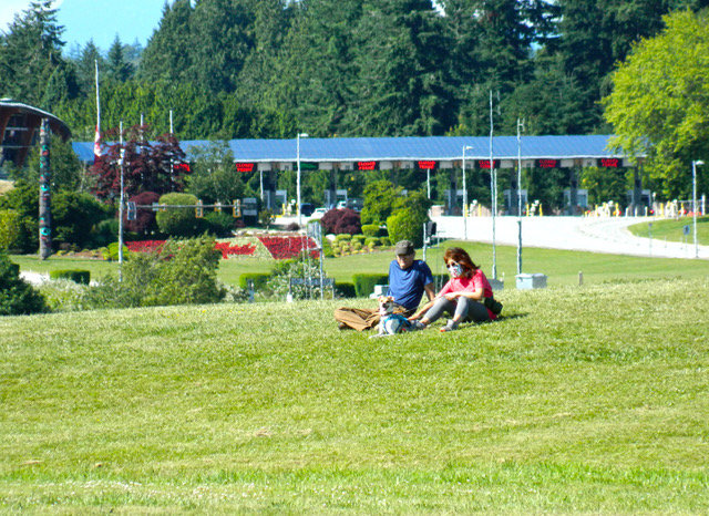 The Canadian flag was recently planted with flowers at the Canadian side of the Peace Arch border crossing near where two people sit June 17.