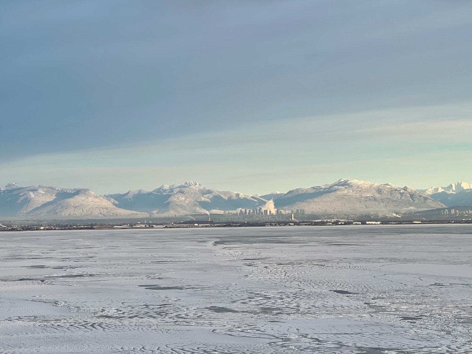 Vancouver’s North Shore mountains appear in the distance past an ice-covered Maple Beach and Boundary Bay. Center, the Metrotown complex in Burnaby.