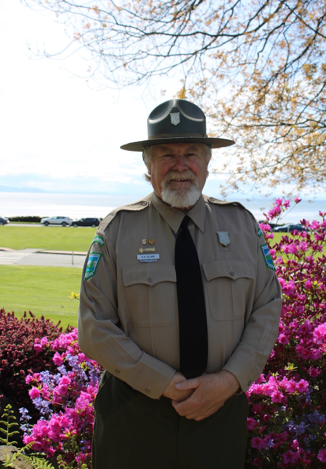 Peace Arch Historical State Park ranger Rickey Blank stands in front of a blooming garden at the park. Blank celebrates 50 years with Washington State Parks on June 1.