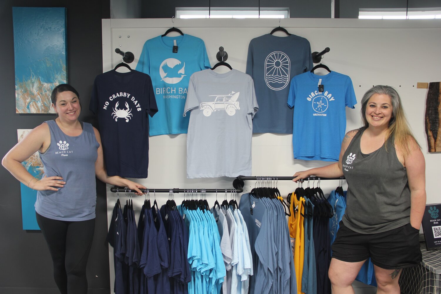 Beach Cat Prints employees Eliza McElroy, l., and Dez Sanguinetti in front of Birch Bay merchandise for sale at the new print shop, located in unit 104 at 4823 Alderson Road.