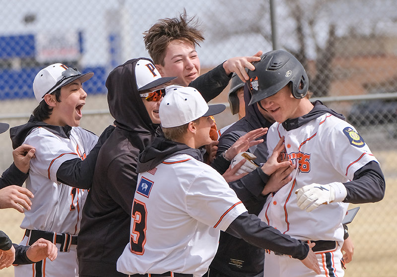 The Pioneer dugout swarms Trey Stenerson as he crosses home plate after hitting Powell&rsquo;s lone home run on Saturday. Stenerson was hit by a pitch in the second game to drive in the winning run, as the Pioneers started the season 2-0 in dramatic fashion.