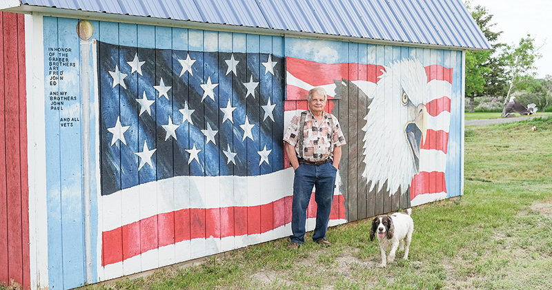 Gary Graber stands with the mural he designed. The mural was a Father&rsquo;s Day surprise for Gary&rsquo;s father, John, as well as a tribute to all veterans for their service. On Flag Day in June, the Sons of the American Revolution awarded Graber a Flag Appreciation Award for showing &lsquo;exemplary patriotism in the display of the flag of the United States.&rsquo;