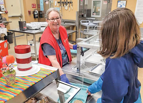 Carrie Satterwhite wears her red vest which signifies foster grandparents and serves lunch to children at Westside Elementary School.