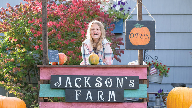 RaeAnn Jackson flashes a big smile at her pumpkin stand on Friday. Jackson has set up shop in her grandmother&rsquo;s front yard on South Bernard Street where she is selling pumpkins, baked goods and cornstalks.
