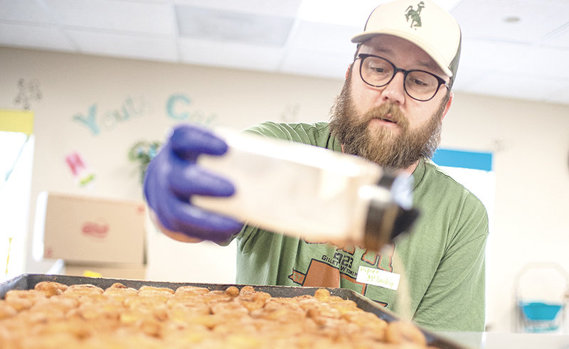 Paul Utzman sprinkles sugar and cinnamon onto a tray of doughnuts fresh from the fryer in the kitchen of the YES House on March 17 in Gillette.