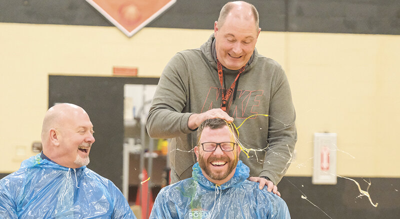 Assistant Superintendent of Teaching and Learning Jason Sleep (left) laughs as middle school teacher Brian Bonander smashes a raw egg down on Superintendent Jay Curtis&rsquo;s head.
