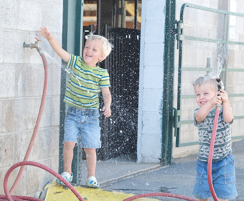 Rhenn Goolsbey (left) and brother Ryatt enjoy playing with the hose at the livestock barns while their brothers Russell and Rhett (not pictured) participate in the cat show on Wednesday.