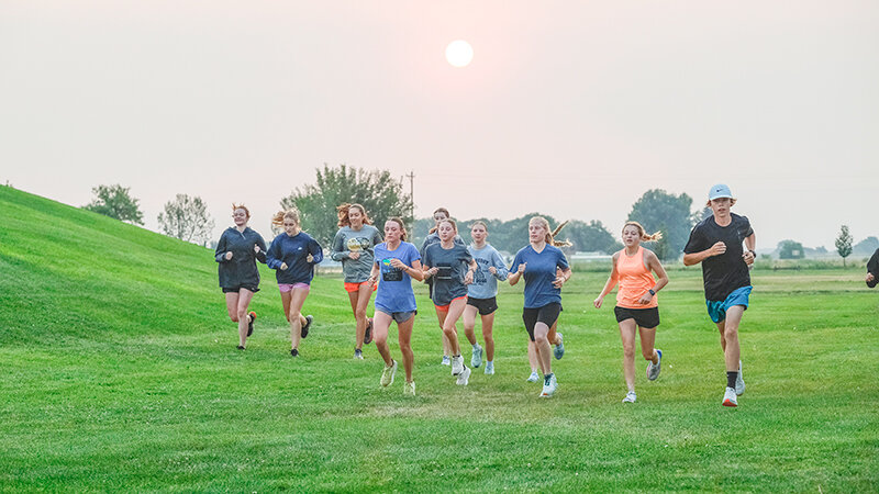 Members of the Panther cross country team warm up under a red sun early in the morning on Thursday last week as smoke settled around Powell.