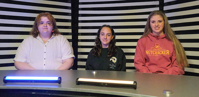 Mia McMinn (left) sits at Cody High School&rsquo;s CHS Wired news desk alongside Eliza Spencer and Kinsley Merritt. Alongside their peers, the students worked on two short films that tackled international and local issues. Both films were shown at the All American High School Film Festival in New York.