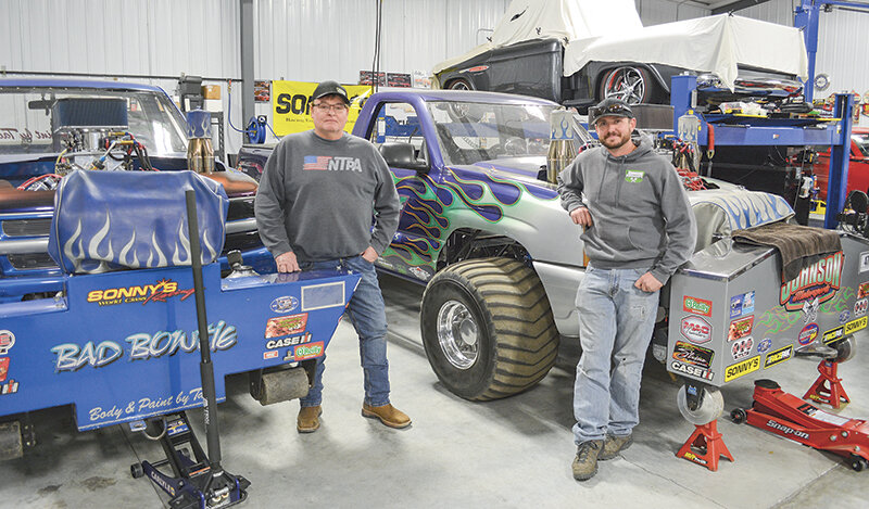 Rick Johnson (left) and Kory Johnson pose beside their trucks, Bad Bowtie and Mr. Awesome, inside the Johnson Motorsports shop. The father and son travel East each summer to compete in truck pulls and have seen strong results.