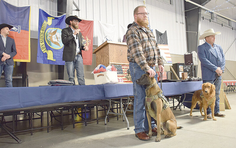 K9 Elite owner Wes Mangus speaks during Saturday night&rsquo;s fundraising banquet alongside, from left, auctioneer Andy Schwab and previous service dog recipients Brandon Tillman and Greg Maynard. K9 Elite is a Lovell-based foundation training dogs to give for free to service men and women who struggle with PTSD or trauma.