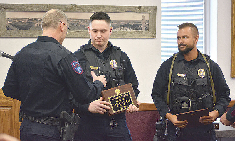 Powell Police Officer Isaac Gutierrez prepares to accept a handshake from Chief Jim Rhea (at left) during Monday night’s Powell City Council meeting, as Officer Kevin Bennett (at right) looks on. Bennett and Gutierrez were honored for their efforts to safely evacuate a Beckman Street apartment complex during a February fire.