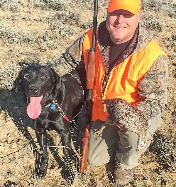 Tribune columnist Mark Davis poses with Gage, a pointing Lab owned by Karl Bear, and his first ever sage grouse during the season last month.