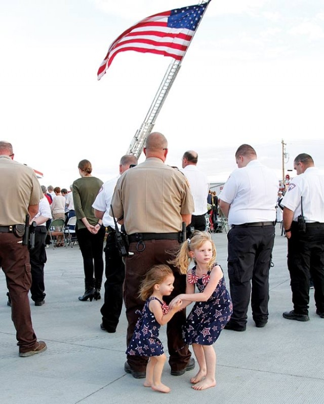 Emma Jones, 2, (left) and her sister, Haleigh Jones, 6, stand behind their dad, Park County Sheriff’s Deputy Aaron Jones, as heads bow at the conclusion of the 9/11 commemoration in Powell. About 150 people attended the ceremony at the Powell Fire Hall on Sunday.