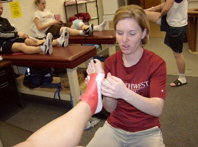 With training room tables filled with student-athletes behind her, Northwest College head athletic trainer Liz Flom tapes an ankle. Flom and the other members of the NWC athletic training office handle the needs of roughly 150 student-athletes throughout the school year.