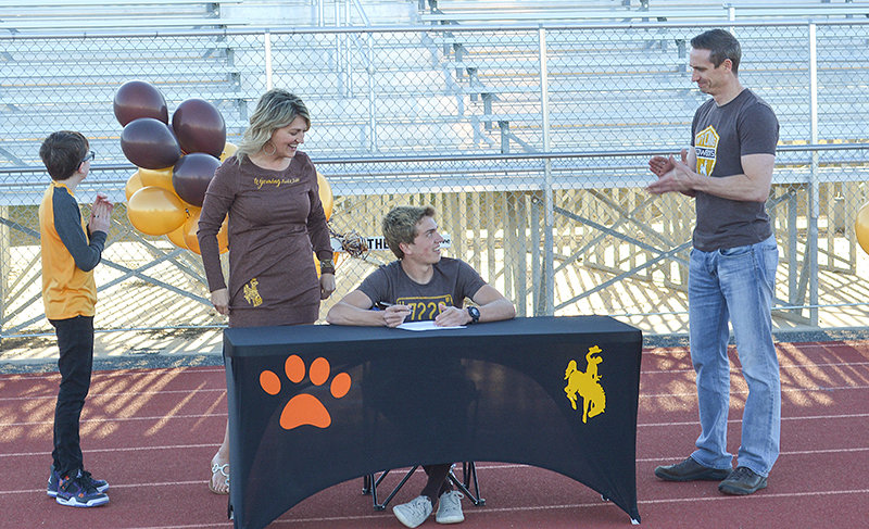 Flanked by his brother Paul, mother Phoebe and father Chris, Jay Cox signs papers officially committing him to the University of Wyoming track team on Tuesday night at Panther Stadium.