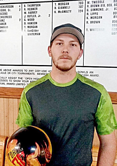 Ty Whiteman poses for a photo at Cody’s Superbowl Lanes and Lounge, flanked by a scoreboard featuring his recent 300 game and 820 and 807 series.
