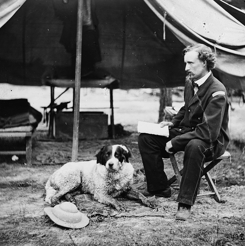 This photograph of George Armstrong Custer was taken during the summer of 1862 in camp. A dog lounges on a rug.
