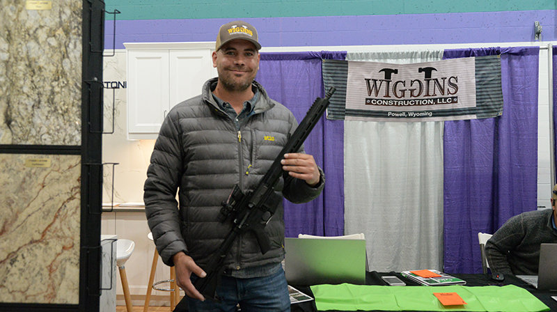 Matt Thomas, customer relations and marketing manager with Wiggins Construction, holds one of the AR-15 rifles the company is giving away with new commercial and residential roofs, during the Home and Garden Show in Cody on Friday.