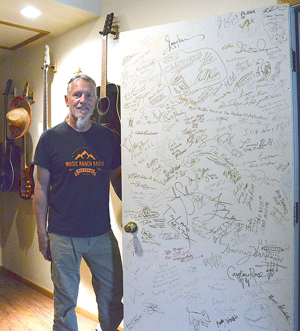 Music Ranch Radio DJ and geologist Greg “Rock Star” Creasy stands next to the door of Jimmy’s Roadhouse, a 40-seat live venue in the Music Ranch Radio studio. The door shows off the signatures of the dozens of musicians the venue has hosted.